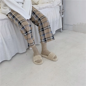 Close-up of cozy plaid pajama pants paired with soft plush slippers on white bedding