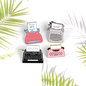 Detailed view of four vintage typewriter enamel pins in red, grey, black and pink colors