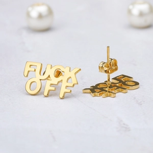 Detailed view of gold FUCK OFF letter stud earrings on a textured marble background