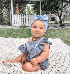 Detail of baby grey romper with ruffle sleeves and blue waffle bow headband on a white blanket