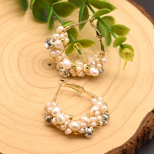 Dettaglio di orecchini a cerchio in filo d'oro con perle e strass su base in legno