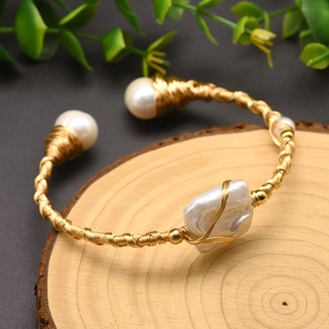 Detail of handmade baroque pearl bangle featuring gold wire wrapping on a wood background