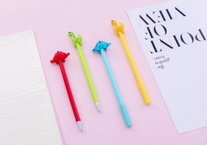 Close-up of four colorful silicone dinosaur cartoon pens on a soft pink desk background