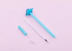 Disassembled view of blue cartoon dinosaur gel pen with cap and refill on pink background