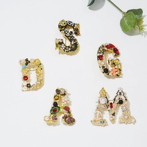 Close-up of baroque letter brooches with pearls and colorful rhinestones on gold alloy