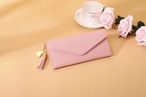 Pink faux leather wallet with heart pendant, tassel detail, and envelope flap design