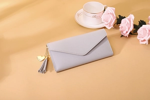 Detail of light gray textured wallet with gold heart pendant and leather tassel