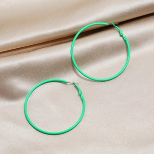 Macro shot of green neon hoop earrings on luxury champagne silk fabric background
