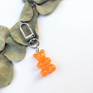 Detailed view of orange resin gummy bear keychain with silver metal clasp on eucalyptus leaves