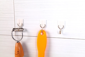 Detail of white plastic adhesive hooks on tiled wall holding kitchen utensils
