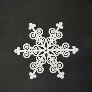 Detail of white plastic snowflake pendant with intricate filigree cutouts on black background