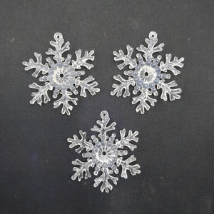 Three clear plastic snowflake ornaments with textured details on a black background
