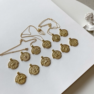Detailed view of 12 baroque zodiac coin necklaces with vintage gold finish on white