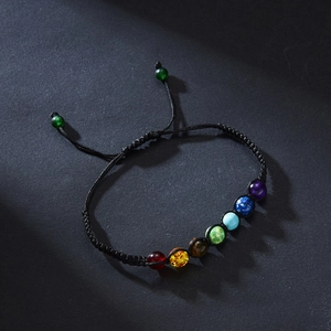 Detail of adjustable black woven bracelet featuring vibrant seven chakra beads on dark background