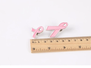 Detailed comparison of small and large pink ribbon breast cancer awareness pins with ruler
