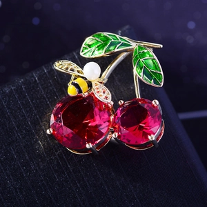 Macro detail of red cherry brooch with enamel leaves and a tiny pearl bee ornament