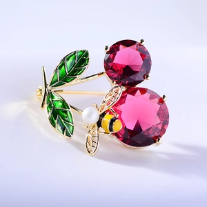 Macro detail of red crystal cherry brooch with enamel leaves and a pearl bee charm