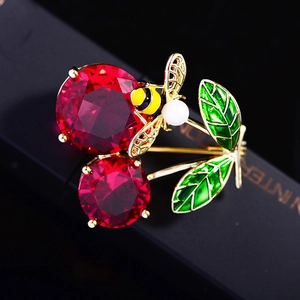 Detailed close-up of cherry brooch with red crystals, green enamel leaves and bee detail