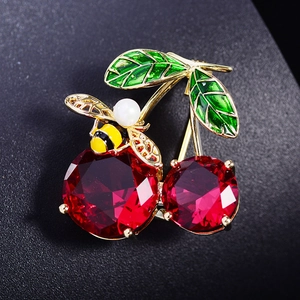 Macro shot of red cherry brooch with green enamel leaves and golden honeybee detail