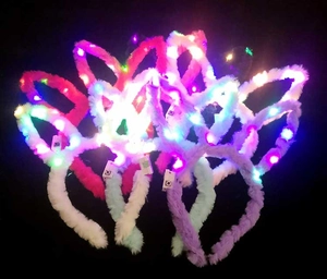 Detail von sieben Plüsch-LED-Hasenohren-Stirnbändern die in Pink Weiß und Lila leuchten