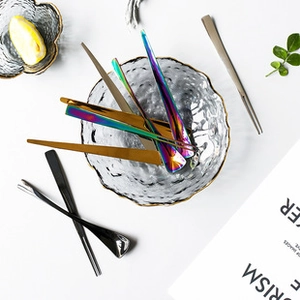 Polished stainless steel spoons and chopsticks in various colors inside a glass bowl