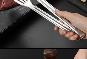Gros plan d'une pince de cuisine en acier inoxydable saisissant de la viande crue