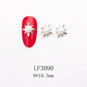 Detail of sun-shaped nail art jewelry with pearl inlay and silver metal rays on red nail