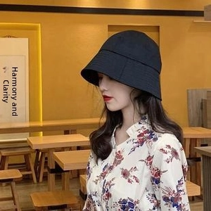 Side view of a black wide-brim cotton bucket hat for women in a cozy teahouse setting