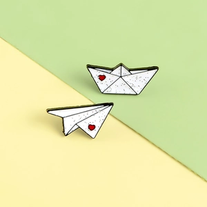 Cute enamel origami boat and airplane brooches with red heart accents on pastel background