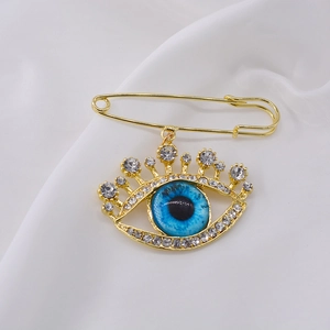 Golden Evil Eye brooch with blue eye and rhinestones on white fabric backdrop