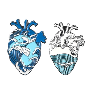 Creative anatomical heart enamel pins with blue ocean waves and whale designs