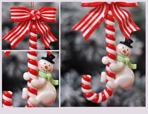 Detail of Christmas candy cane ornament with snowman figure on green tree branch