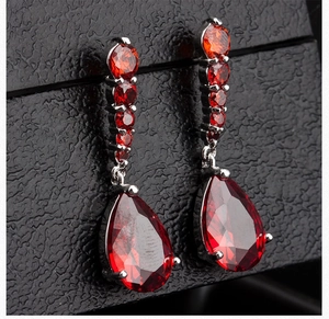 Detailed macro view of gunmetal earrings with red teardrop and round cut cubic zirconia