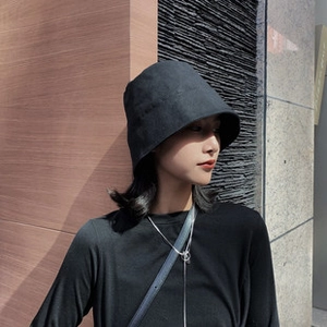 Close-up of black cotton sun visor hat worn by a model against a minimalist building wall