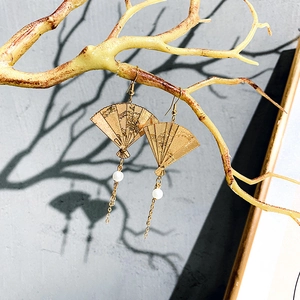 Close-up of golden fan-shaped earrings with tassels and pearls on a dry branch