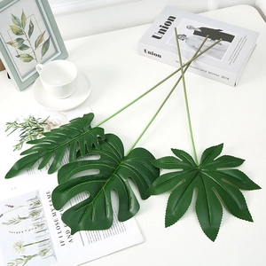 Detail of three artificial dark green leaves with long stems on a clean white desk setup