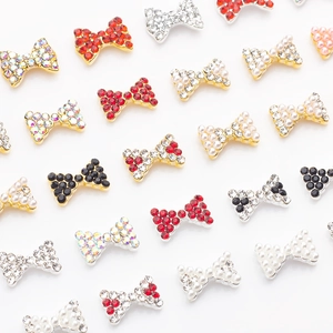 Mise à plat de breloques nœuds pour nail art avec strass rouges et perles sur fond blanc