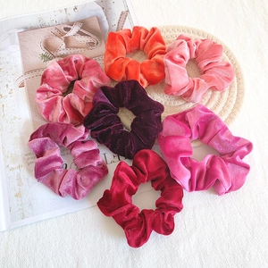 Close-up of velvet scrunchies in warm tones including burgundy and coral on a textured background