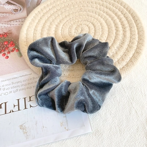 Detail of grey velvet scrunchie placed on a textured beige woven mat background