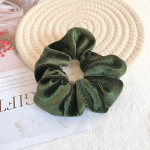 Macro view of dark green corduroy velvet scrunchie on a decorative woven mat