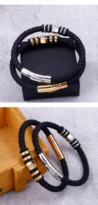 Close-up of black braided leather bracelets with gold and silver steel charms on wood box