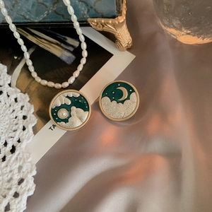 Macro detail of retro gold earrings with green enamel, moon and cloud patterns on silk