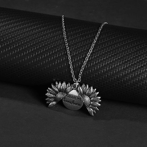 Detailed view of silver sunflower necklace with You Are My Sunshine engraving on black background