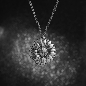 Silver sunflower locket necklace with detailed petal textures on a dark background