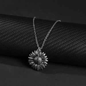 Detailed view of silver sunflower pendant necklace hanging on a textured dark pedestal