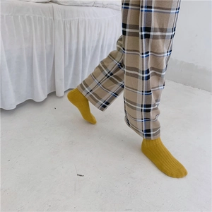 Detail of yellow ribbed wool blend socks worn with plaid pants in a cozy lifestyle setting