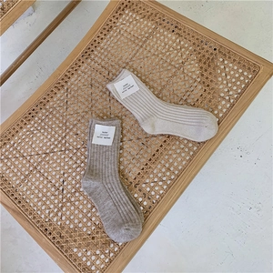 Close-up of thick ribbed wool socks with brand labels on a woven rattan surface