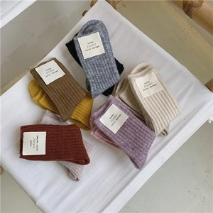 Pile of seven colorful thick wool rib knit socks on a wooden chair with canvas seat