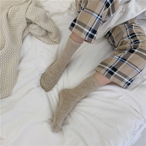 Close-up of khaki wool blend socks with cable knit texture on a cozy white bed