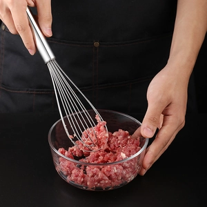 Manual stainless steel whisk mixing meat filling in a glass bowl, modern kitchen tool